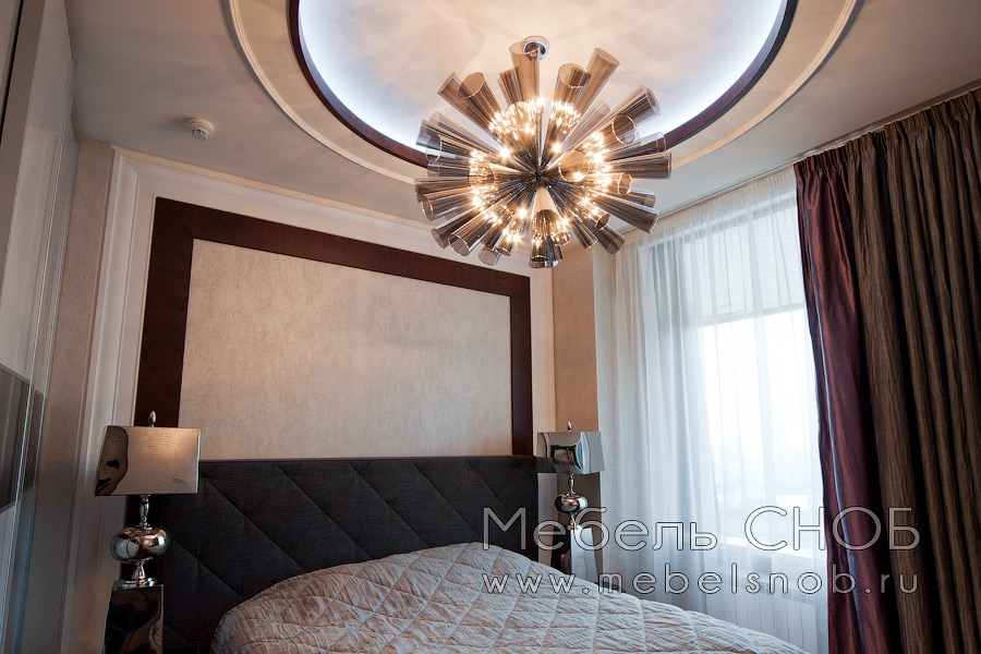 Дизайнерская люстра и хромированные прикроватные светильники эффективно дополняют интерьер спальни.